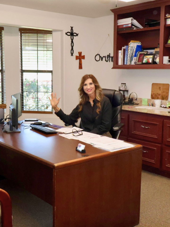 Christine waving from her desk at Brenham Insurance